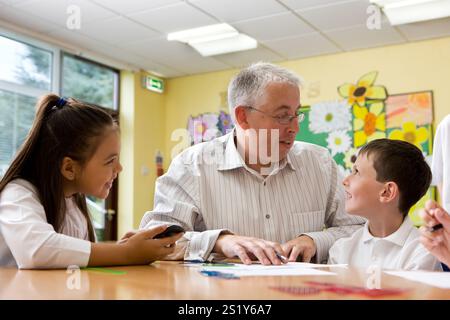 Scuola junior: Insegnante e alunni. Un paio di bambini delle scuole medie che lavorano alla loro scrivania mentre l'insegnante offre alcuni suggerimenti costruttivi. Foto Stock