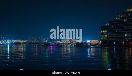 Yas Island vista da al Raha ad Abu Dhabi, Emirati Arabi Uniti, con il suo skyline illuminato e le luci riflesse sul tranquillo lungomare. La scena capt Foto Stock