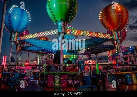 Giostra di carnevale illuminata di sera, con colori vivaci, luci e un'atmosfera festosa. I bambini si godono l'esperienza di un capriccio Foto Stock