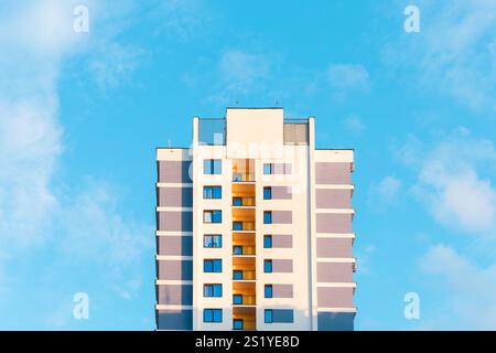 Alto e moderno edificio residenziale. Alto condominio urbano con balconi gialli e grandi finestre su una facciata testurizzata, adagiata contro un cielo nuvoloso. Contem Foto Stock