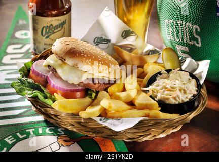 "Hamburger di manzo con patatine fritte, insalata e una bottiglia di birra, servito in un cestino: Un pasto delizioso e soddisfacente." Foto Stock