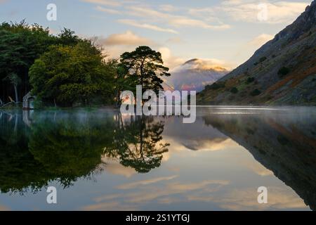 La luce del sole di prima mattina colpisce Great Gable mentre le nuvole iniziano a sgombrarsi dalla cima, riflessa nelle acque nebbiose e calme delle acque reflue nel Lake Dist Foto Stock