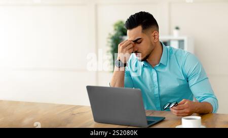 Millennial imprenditore arabo che ha stancato gli occhi irritati, overworking su laptop, esaurito dal lavoro online in ufficio Foto Stock