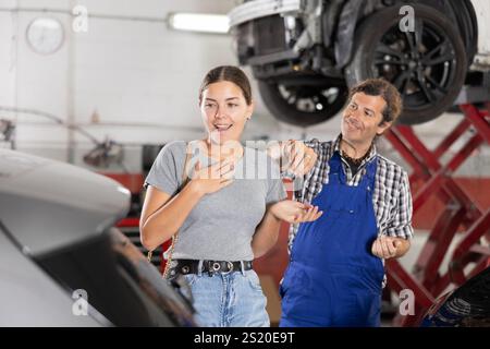 Cliente donna felice che riceve la chiave dell'auto dal meccanico dopo la riparazione Foto Stock