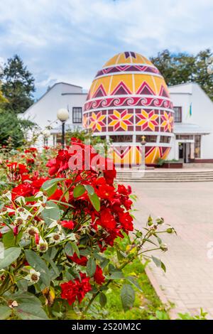 Un grande edificio a forma di uovo con decorazioni rosse e gialle. Di fronte all'edificio si trova un giardino fiorito Foto Stock