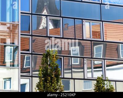 La conversione in loft di un edificio residenziale si riflette nella facciata di vetro di un moderno blocco di uffici Austria Foto Stock