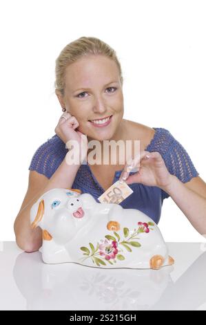 Una giovane donna di fronte a uno sfondo bianco con un salvadanaio. Risparmiare denaro per la vecchiaia. Austria Foto Stock