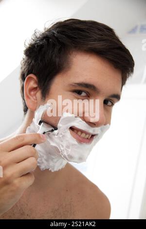 Il giovane uomo si rade con la lama del rasoio e la schiuma da barba nel bagno Austria Foto Stock