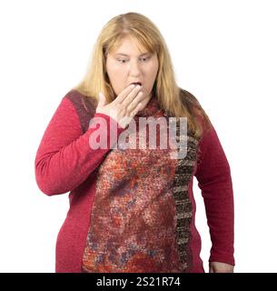 Una donna con lunghi capelli biondi viene catturata in una posa sorpresa, coprendo la bocca con una mano. Indossa un maglione rosso con motivi geometrici, in piedi Foto Stock