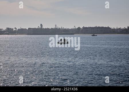 San Diego, California, Stati Uniti. 21 dicembre 2024. Un piccolo gruppo di persone gode di una tranquilla escursione di pesca in una piccola barca sulle calme acque della baia di San Diego. La sagoma dei pescatori è posta contro i riflessi scintillanti della luce del sole sull'acqua, con la costa di Coronado e gli edifici residenziali che forniscono uno sfondo sereno. Questa tranquilla scena mette in risalto il lato ricreativo della Baia di San Diego, dove il tempo libero e la natura si intersecano nel cuore del vivace lungomare. (Credit Image: © Ian L. Sitren/ZUMA Press Wire) SOLO PER USO EDITORIALE! Non per USO commerciale! Foto Stock