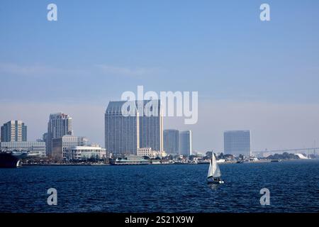 San Diego, California, Stati Uniti. 21 dicembre 2024. Una barca a vela scivola con grazia attraverso la baia di San Diego, annidata dall'impressionante skyline della città. Le iconiche torri gemelle del Manchester Grand Hyatt dominano la scena, fiancheggiate da altri edifici moderni e dal San Diego Convention Center sullo sfondo. Le scintillanti acque blu della baia contrastano con lo skyline urbano, mentre il ponte Coronado sbircia attraverso l'orizzonte nebuloso all'estrema destra. Questo tranquillo momento marittimo cattura la miscela di bellezza naturale e vivace vita urbana che caratterizza San Diego. (Immagine di credito: © Ian L. Sitren/ZUMA Press Wi Foto Stock