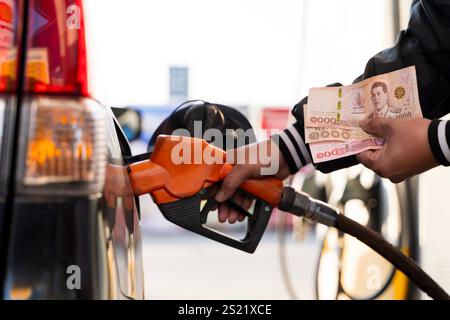 Uomo con banconote al distributore di benzina. Mano d'uomo che mette i soldi nel serbatoio dell'auto, primo piano, concetto di carburante costoso, crisi del carburante Foto Stock