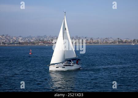 San Diego, California, Stati Uniti. 21 dicembre 2024. Un'elegante barca a vela scivola attraverso la baia di San Diego, le sue vele bianche che si infrangono sullo sfondo della vivace costa della città. Le tranquille acque della baia riflettono le condizioni di calma e brezza, mentre gli occupanti della nave si godono una giornata tranquilla sull'acqua. Il porticciolo e il paesaggio costiero di San Diego offrono un ambiente pittoresco, rendendolo una destinazione popolare per gli amanti della nautica da diporto e della vela. (Credit Image: © Ian L. Sitren/ZUMA Press Wire) SOLO PER USO EDITORIALE! Non per USO commerciale! Foto Stock