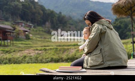 Mote abbraccia sua figlia in un prato al tramonto. Mamma che bacia il suo bambino seduto sull'erba delle Alpi. Abbracciare il concetto di mia mamma. Foto Stock