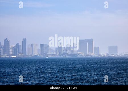 San Diego, California, Stati Uniti. 21 dicembre 2024. Lo skyline del centro di San Diego emerge attraverso una nebbia leggera, creando una vista soffusa ma suggestiva dell'architettura moderna della città. Gli edifici torreggianti sono incorniciati dalle calme acque della Baia di San Diego, con il Ponte Coronado ben visibile in lontananza. Questa suggestiva scena cattura l'interazione tra la vivacità urbana e la tranquillità costiera, mostrando il caratteristico fascino del lungomare di San Diego. (Credit Image: © Ian L. Sitren/ZUMA Press Wire) SOLO PER USO EDITORIALE! Non per USO commerciale! Foto Stock