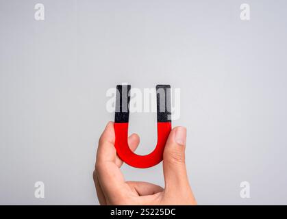 Calamita a ferro di cavallo in mano umana. Persona che tiene una mano con un magnete, colore nero e rosso, isolata su sfondo grigio con spazio di copia. Marketing sui social media Foto Stock