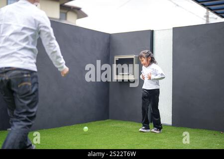 Un genitore e un bambino giapponesi, un uomo di 20 anni e una bambina di 6 anni, giocano lanciando palle di plastica verdi l'uno contro l'altro nel giardino recintato di Foto Stock