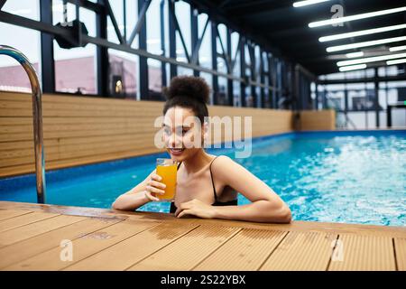 La giovane donna si rilassa presso la piscina termale, sorseggiando un drink all'arancia e godendosi i suoi tranquilli dintorni. Foto Stock