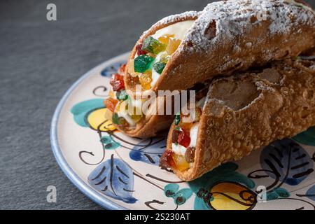 Primo piano di tre cannoli siciliani su un piatto decorato, evidenziando il guscio croccante, il ripieno cremoso di ricotta e il vivace condimento di frutta candita. RIC Foto Stock