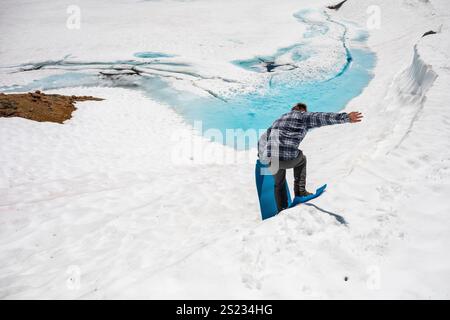 Un uomo sta in piedi su un dormitorio per scivolare giù da una collina verso un lago ghiacciato Foto Stock