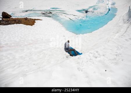 Un uomo sta in piedi su un dormitorio per scivolare giù da una collina verso un lago ghiacciato Foto Stock