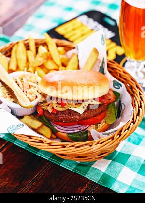 "Hamburger di manzo con patatine fritte, insalata e un bicchiere di birra, servito in un cestino: Un pasto delizioso e soddisfacente." Foto Stock