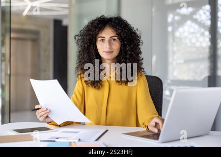 Ritratto di una donna seria e concentrata che fa i documenti in ufficio, una donna d'affari che guarda con attenzione alla fotocamera, lavora con contratti e rapporti finanziari. Foto Stock