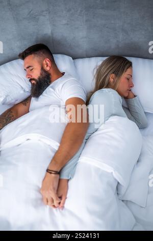 Una giovane coppia sposata sta dormendo nel loro letto. Si tengono per mano e si godono un buon sonno. Foto Stock