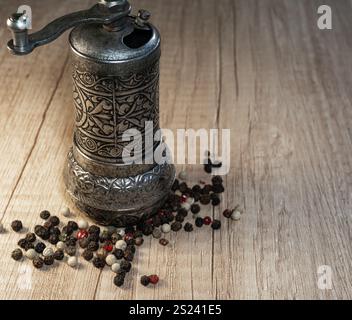 Macinacaffè per spezie e grani di pepe in primo piano. Tritatutto per peperoni con impasto per peperoni su un tavolo di legno. Foto Stock
