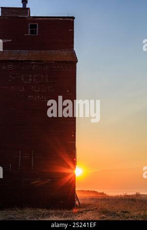 Un edificio in mattoni rossi con una grande finestra e un cartello con la scritta "luce". Il sole tramonta dietro l'edificio, proiettando un caldo bagliore sulla scena Foto Stock
