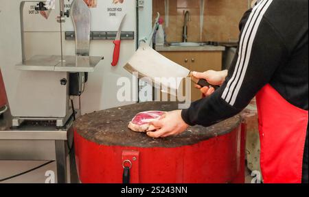 Primo piano delle mani di un macellaio che taglia fette di carne cruda nel suo negozio. Macellaio che taglia carne cruda. Foto Stock