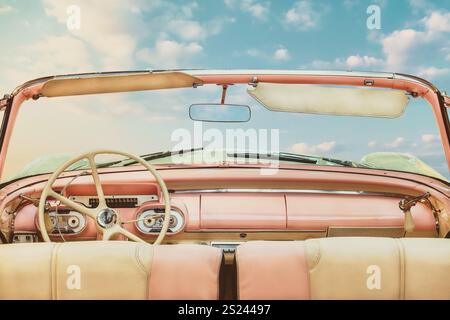 Vista del conducente di una classica cabriolet americana aperta rosa d'epoca di fronte a un cielo azzurro soleggiato Foto Stock