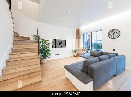 Soggiorno contemporaneo con pavimenti in legno duro, arredi eleganti, completato dalla luce naturale dalle grandi finestre. Ideale per design, interni e. Foto Stock