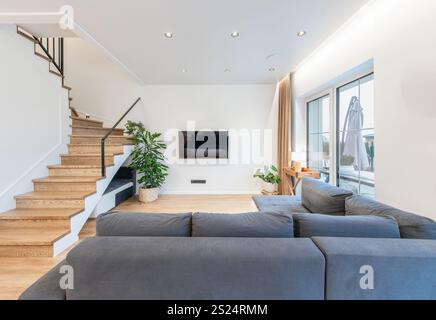 Soggiorno contemporaneo con pavimenti in legno duro, arredi eleganti, completato dalla luce naturale dalle grandi finestre. Ideale per design, interni e. Foto Stock