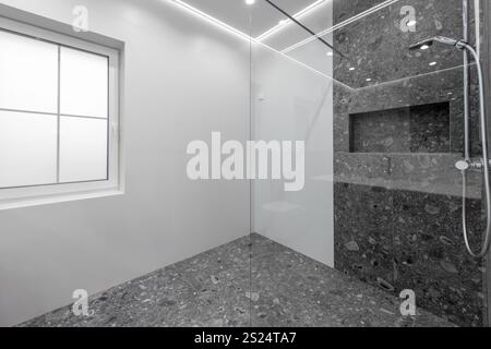 Il bagno dal design contemporaneo presenta eleganti piastrelle grigie, un divisorio per doccia in vetro e una finestra luminosa che sfoggia un mix di stile moderno e functio Foto Stock