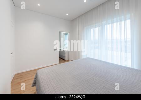 Una tranquilla camera da letto offre illuminazione naturale attraverso grandi finestre, decor minimalista con tende chiare e un'atmosfera pulita. Perfetto per rilassarsi Foto Stock