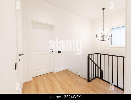 Una casa moderna e minimalista, corridoio con caldo pavimento in legno, elegante scala a rotaia nera, porte a pannello bianco, illuminate da un contempo Foto Stock