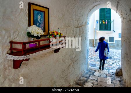 Una donna passeggia sotto un arco di pietra nel centro storico di Monopoli, Italia, mostrando le affascinanti stradine e l'architettura tradizionale della città Foto Stock