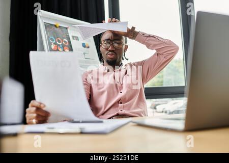 Un giovane afroamericano esamina documenti con un'espressione premurosa in uno spazio di lavoro moderno. Foto Stock