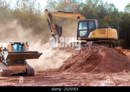 Gli escavatori e i caricatori spostano la terra nel cantiere, creando polvere che preparano il terreno allo sviluppo. Foto Stock