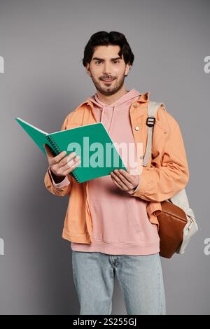 Un giovane e bello uomo con i capelli bruna si regge con sicurezza, tenendo in mano un quaderno. Foto Stock