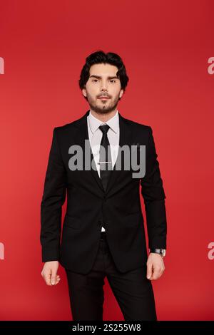 Un giovane con i capelli scuri si erge alto con un abito nero, emanando fascino e sicurezza. Foto Stock