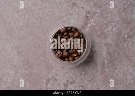 Vista dall'alto dei chicchi di caffè appena tostati aromatici in un piccolo bicchiere su cemento grigio. Miscela arabica e robusta. Copia spazio sfondo, copertina, sfondo Foto Stock