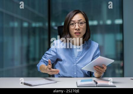 Donna arrabbiata e irritata che guarda la fotocamera, donna d'affari che chatta con i colleghi durante una riunione di lavoro online, vista webcam. Impiegato asiatico sul posto di lavoro. Foto Stock