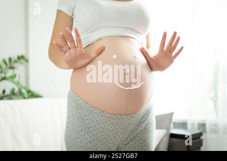 Donna incinta con un sorriso disegnato dalla crema per smagliature sul pancino Foto Stock