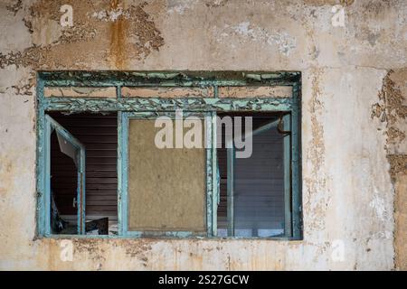 Primo piano di una finestra sbucciata in un edificio abbandonato, caratterizzata da vernice spaccata e una texture rustica e decaduta. Foto Stock