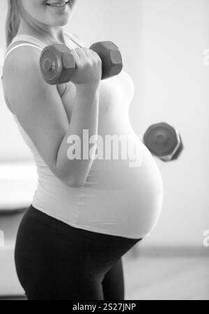 Primo piano foto in bianco e nero di donna incinta che solleva manubri Foto Stock