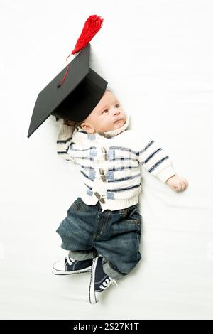 Un bambino carino che giace nel cappello di graduazione sul letto Foto Stock