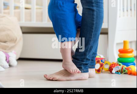 Foto ravvicinata dei piedi del bambino in piedi davanti ai piedi della madre sul pavimento Foto Stock