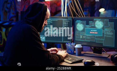 Hacker in un magazzino sotterraneo buio che cerca di rubare dati preziosi rivolgendosi a siti Web governativi, ma riceve un messaggio di errore di accesso negato, respinge gli attacchi informatici, stupido in un colpo ravvicinato Foto Stock